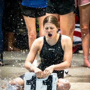 Team mate getting soaked as the swimmer in the water does a flip turn